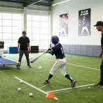 Young athlete training at a hit club batting cage with coach, showcasing dedication and teamwork.