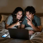 Couple enjoying NSFW AI chat on laptop in cozy bedroom setting.